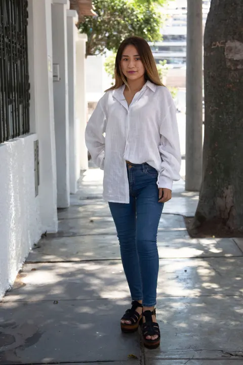 A woman in a white shirt and jeans standing on a city sidewalk.