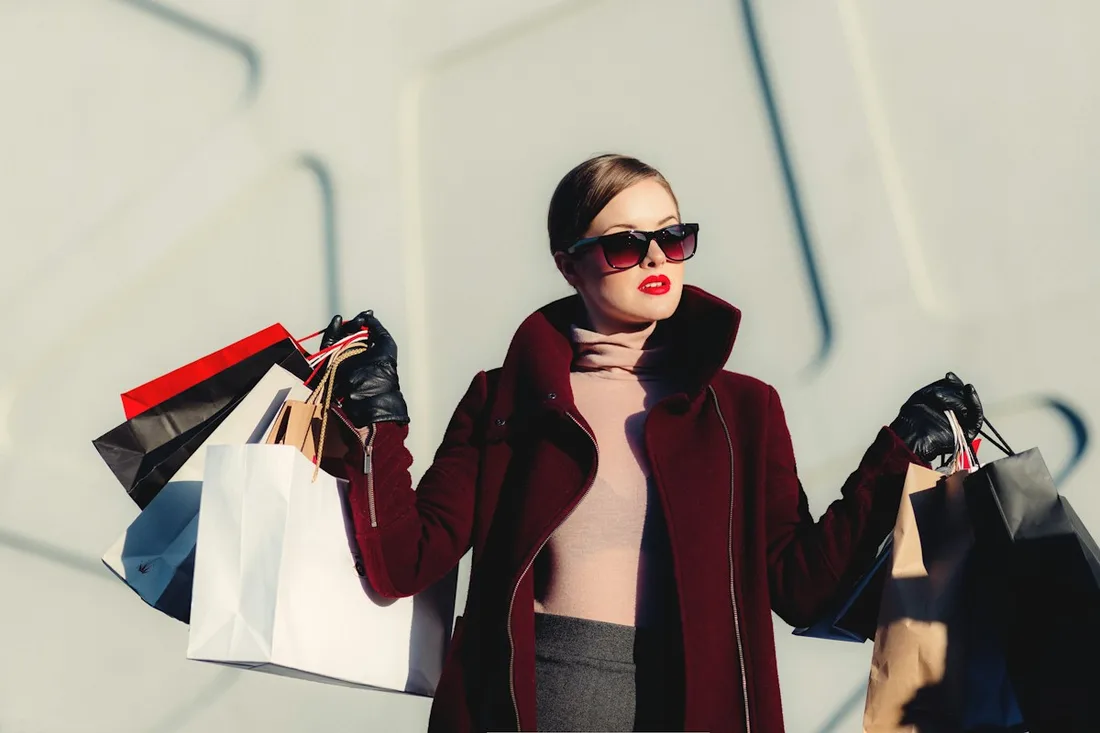 Woman in sunglasses and a dark coat holding shopping bags