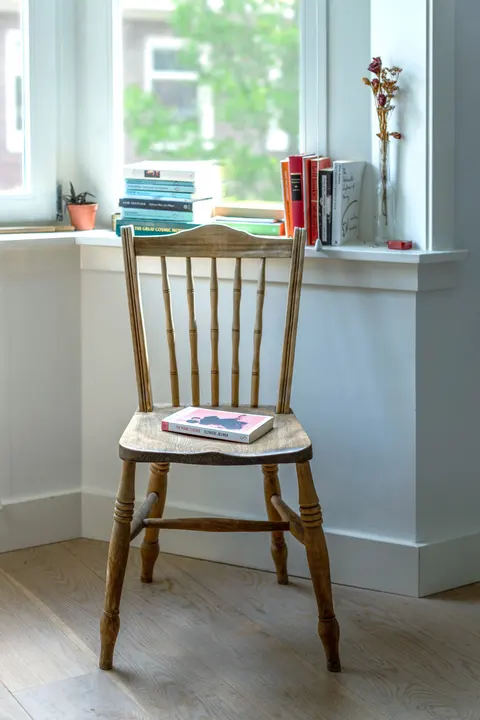 A wooden chair and books arranged by a window in a quiet room.