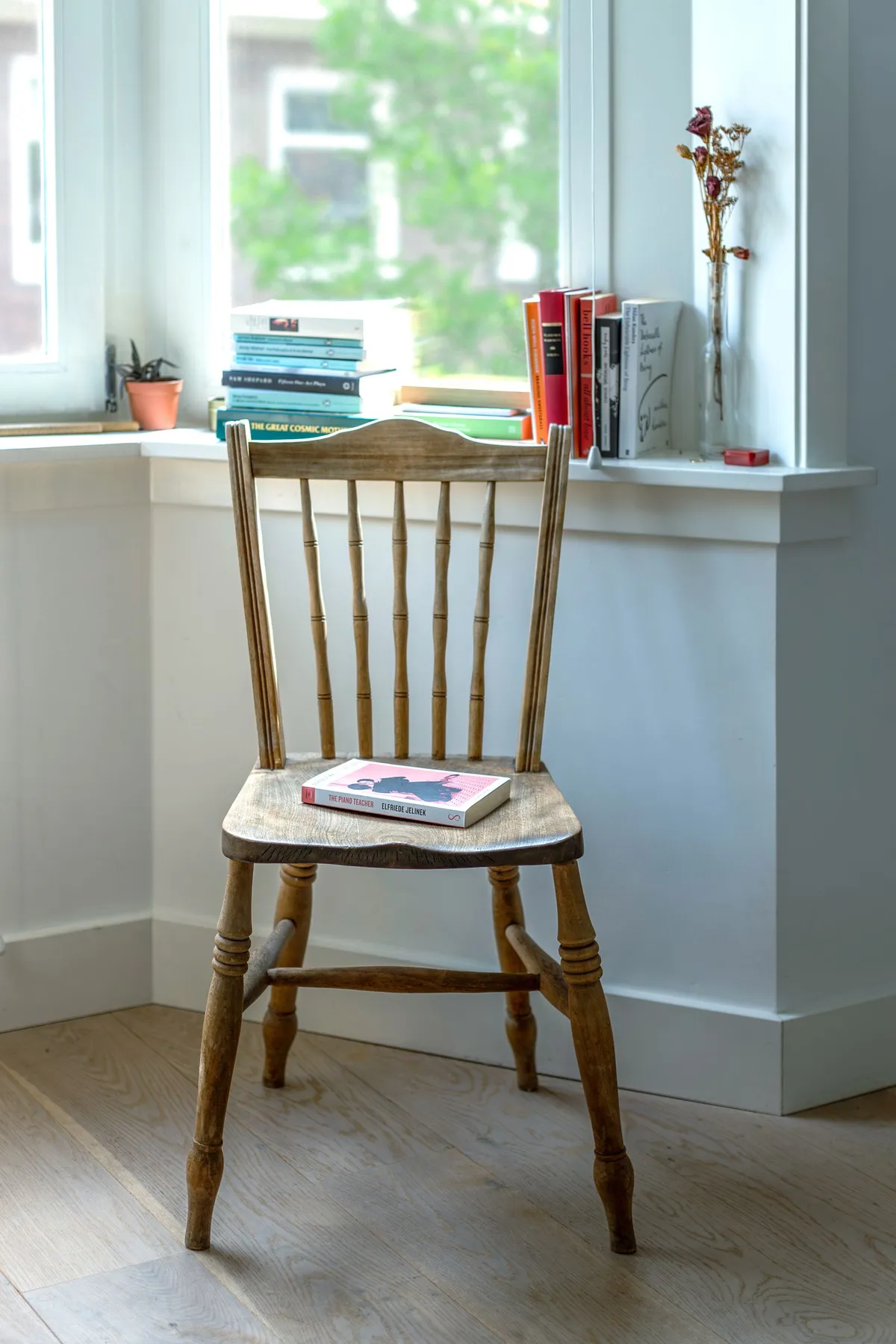 A wooden chair and books arranged by a window in a quiet room.