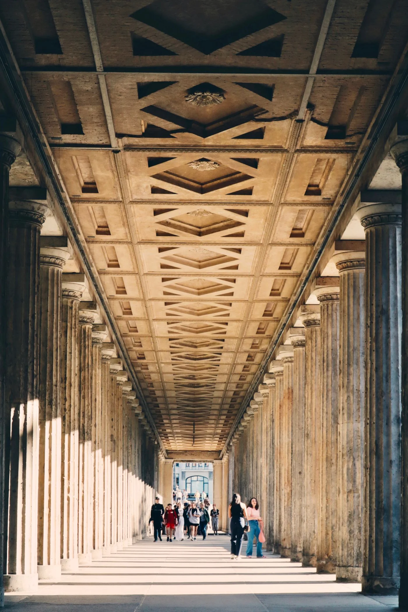 People walking beside the classical colonnade on Museum Island in Berlin.