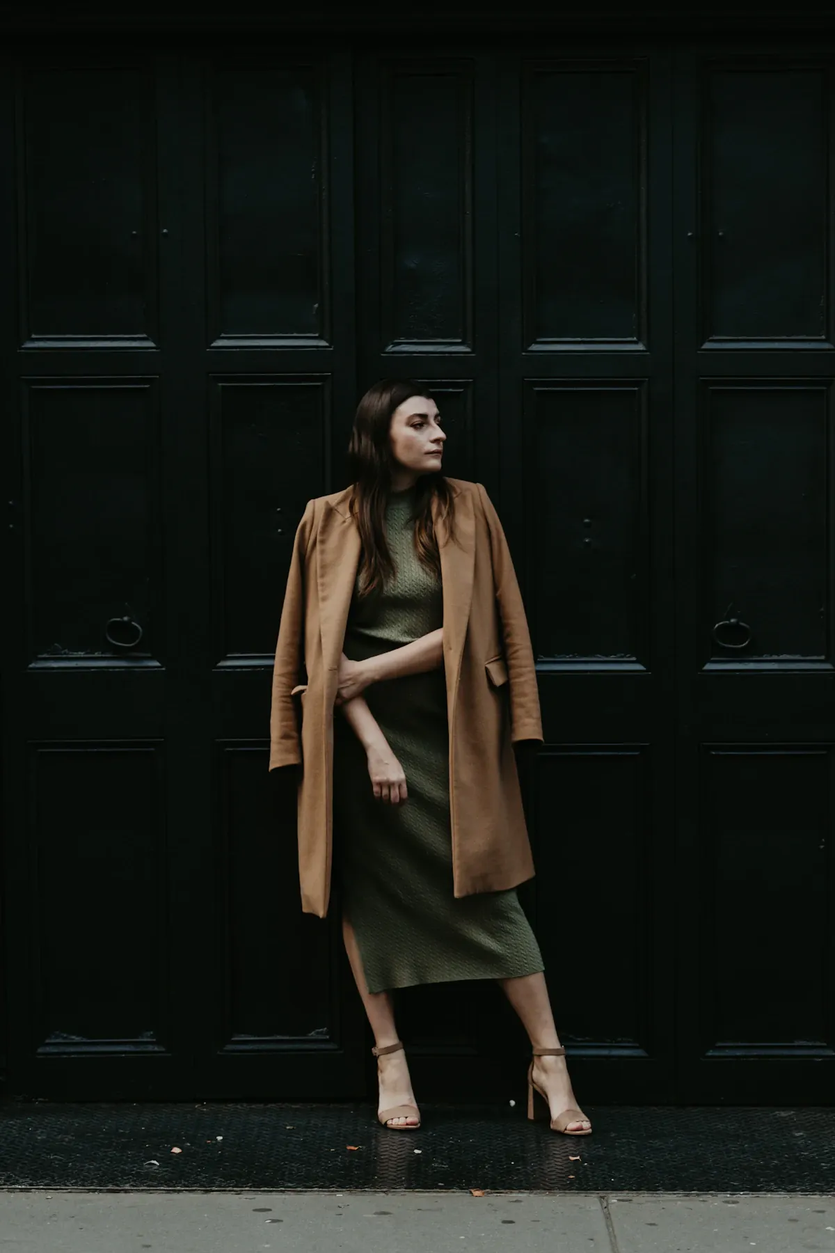 A woman wearing an open tan coat over a dark outfit.